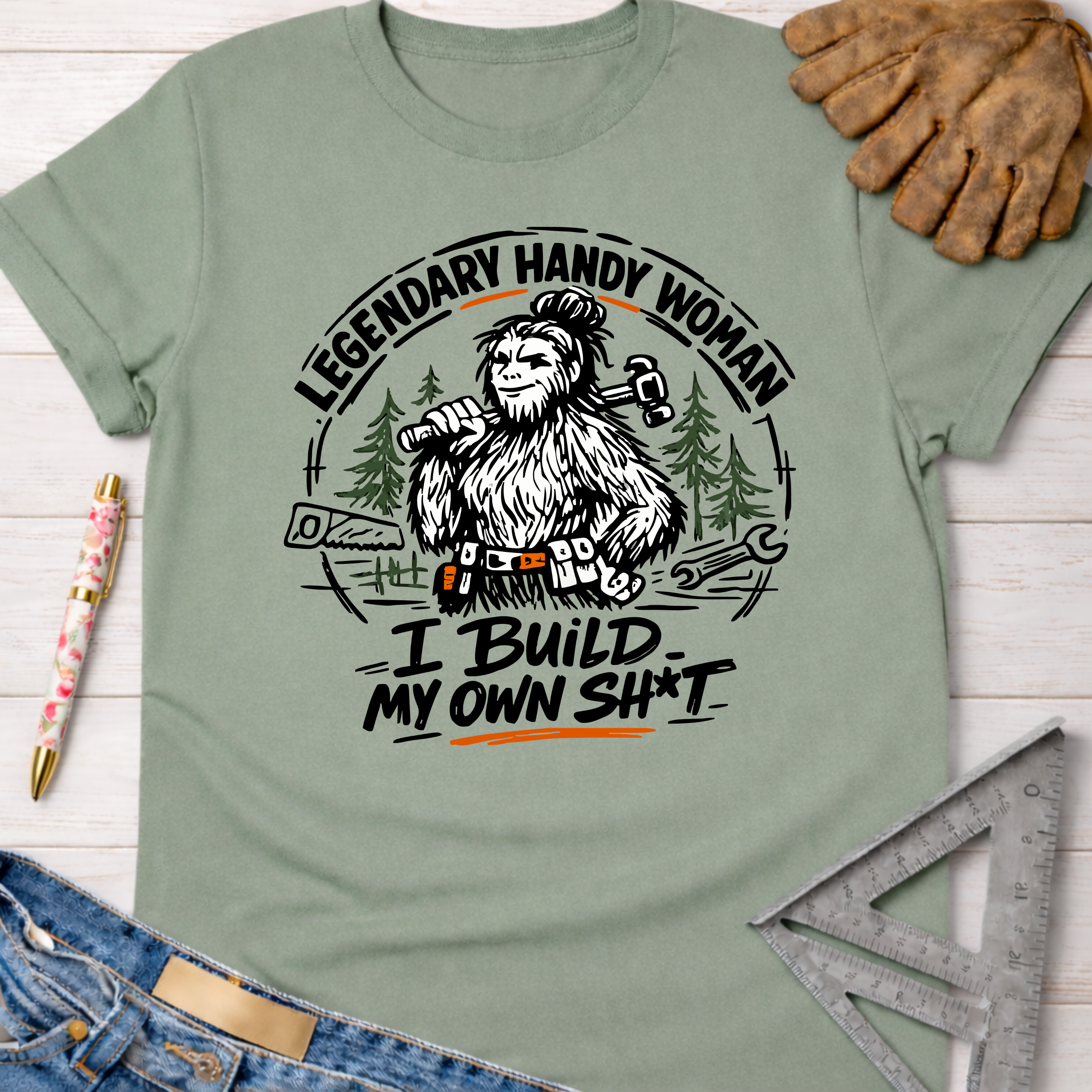 Women's funny woodworking graphic tee shirt for female woodworkers, makers, and DIY builders — Sawdust & Ponytails. Sage green cotton t-shirt with a Bigfoot "Legendary Handy Woman" graphic.