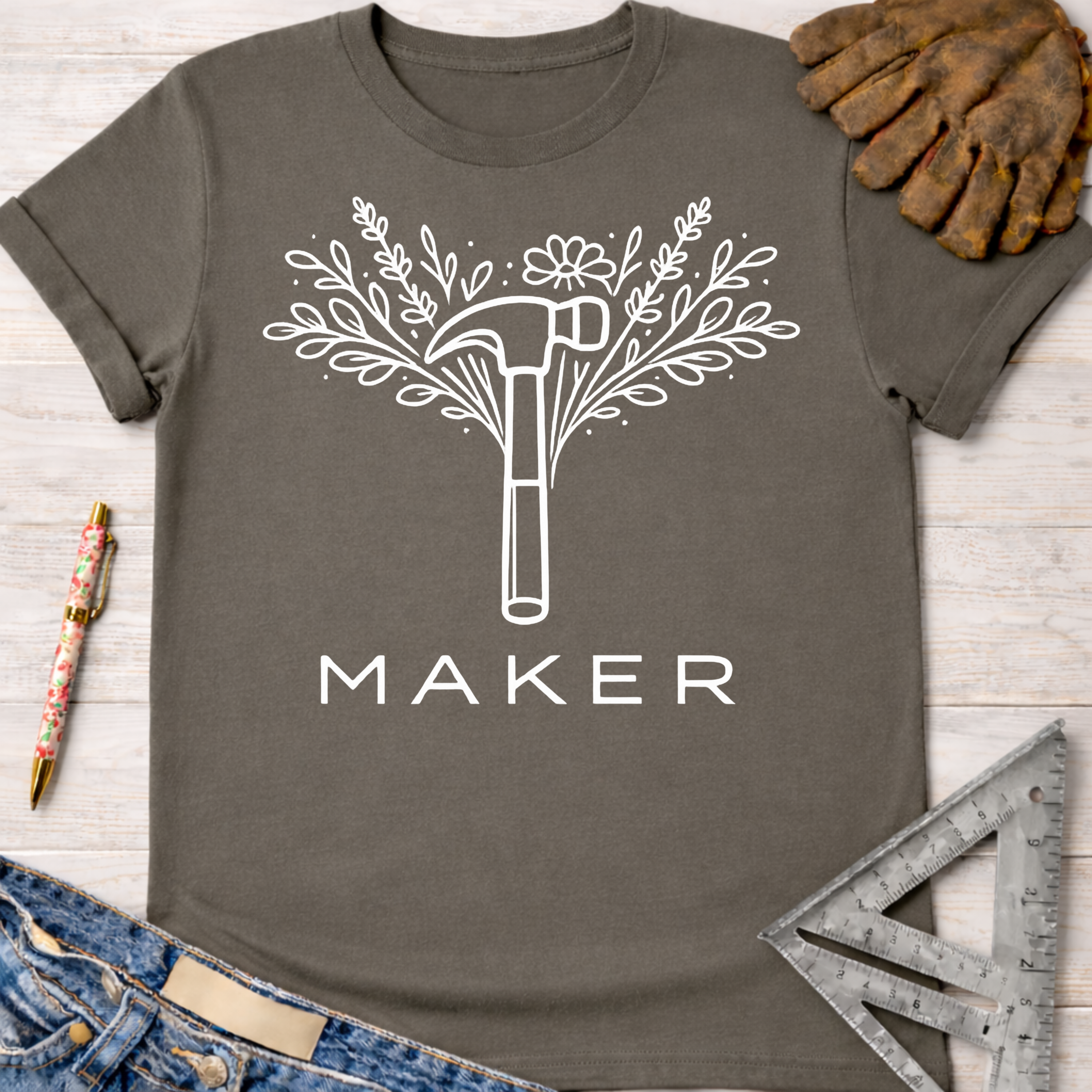 Women's funny woodworking graphic tee shirt for female woodworkers, makers, and DIY builders — Sawdust & Ponytails. Dark gray cotton tee with white floral hammer and "MAKER" graphic.