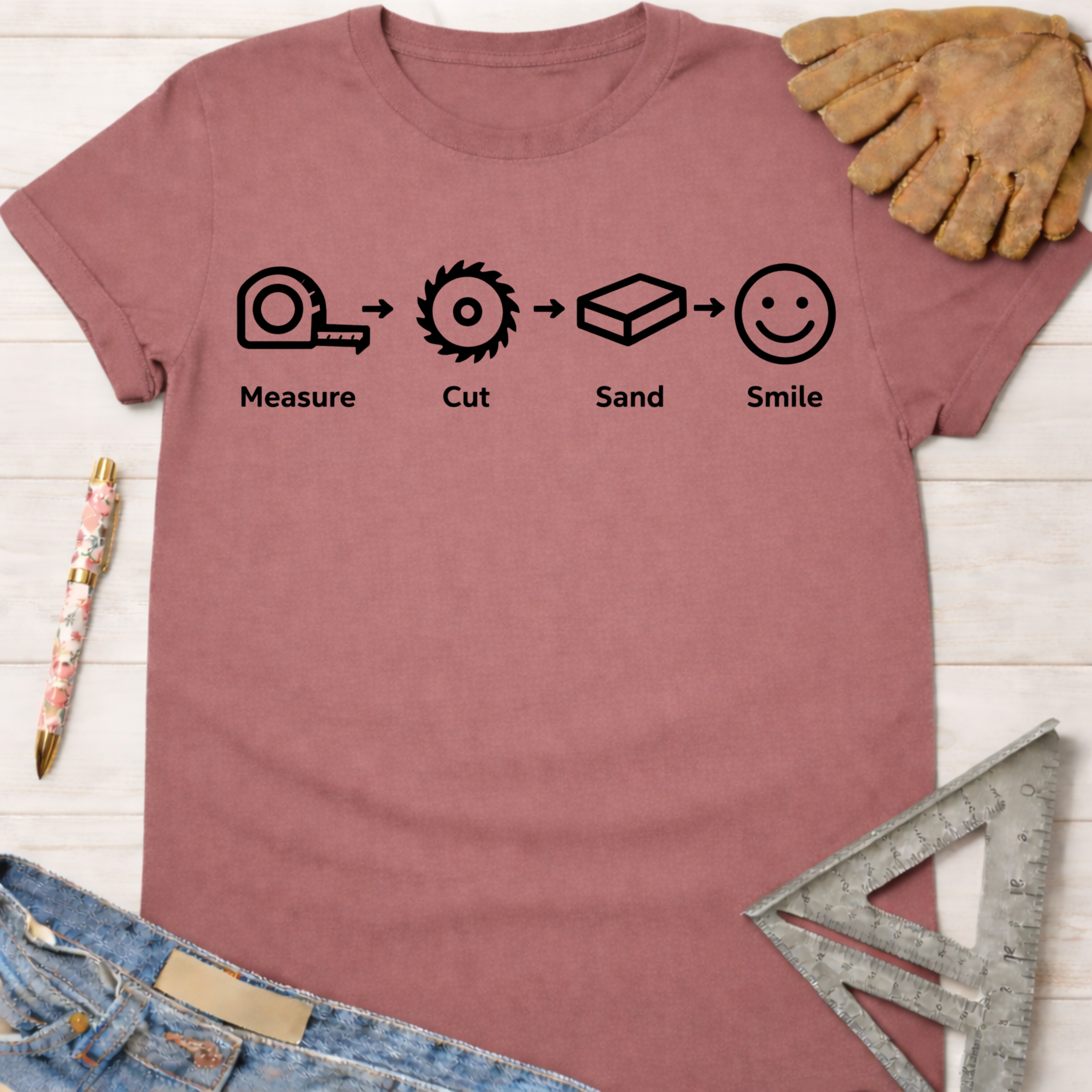 Women's funny woodworking graphic tee shirt for female woodworkers, makers, and DIY builders — Sawdust & Ponytails. Mauve cotton tee with "Measure. Cut. Sand. Smile." graphic.