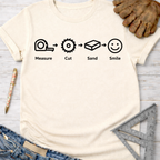 Women's funny woodworking graphic tee shirt for female woodworkers, makers, and DIY builders — Sawdust & Ponytails. Cream t-shirt with "Measure. Cut. Sand. Smile." icons.