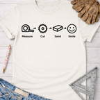 Women's funny woodworking graphic tee shirt for female woodworkers, makers, and DIY builders — Sawdust & Ponytails. White cotton t-shirt with "Measure. Cut. Sand. Smile." graphic.