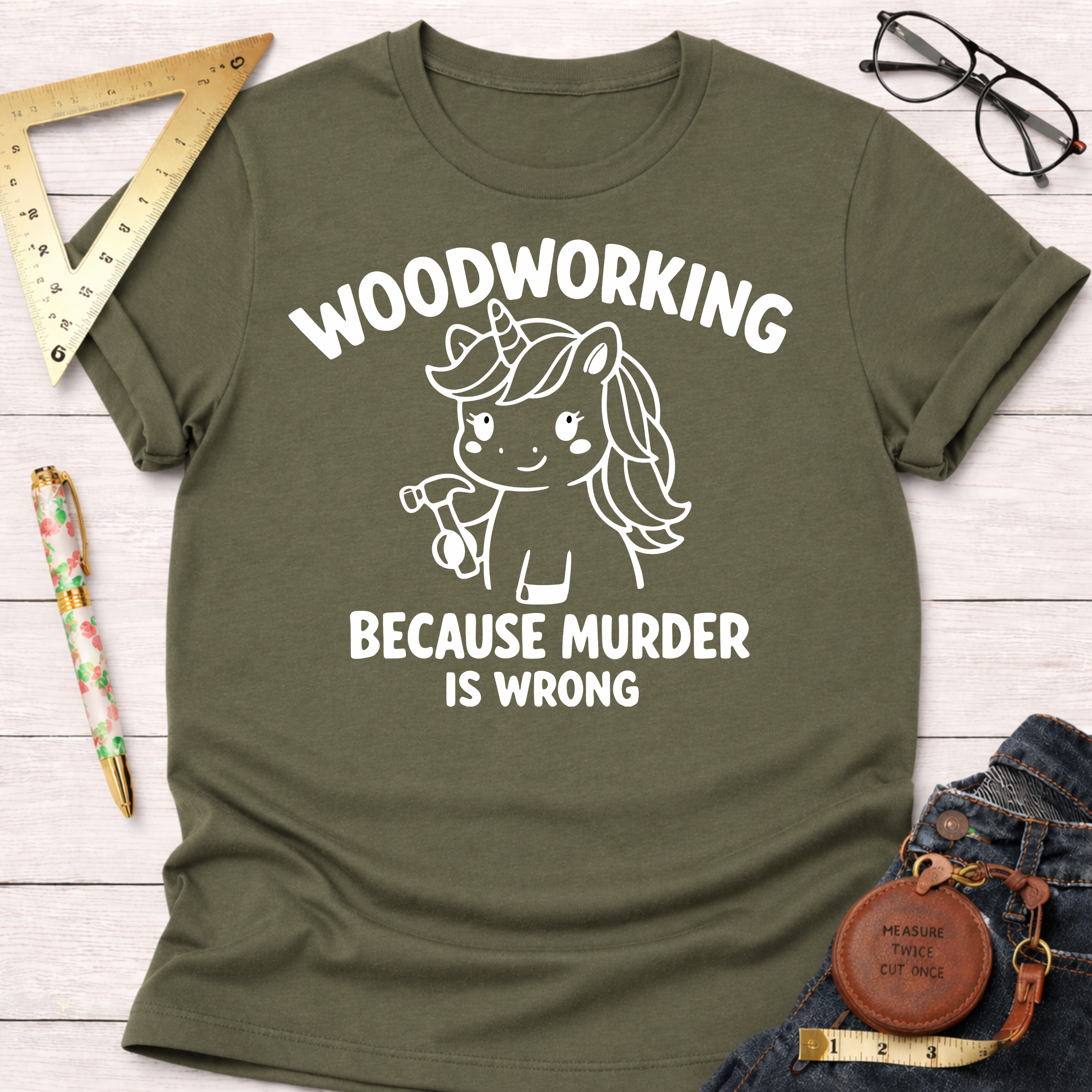 Women's funny woodworking graphic tee shirt for female woodworkers, makers, and DIY builders — Sawdust & Ponytails. Olive green cotton tee with a white unicorn holding a hammer and "Woodworking Because Murder Is Wrong" text.