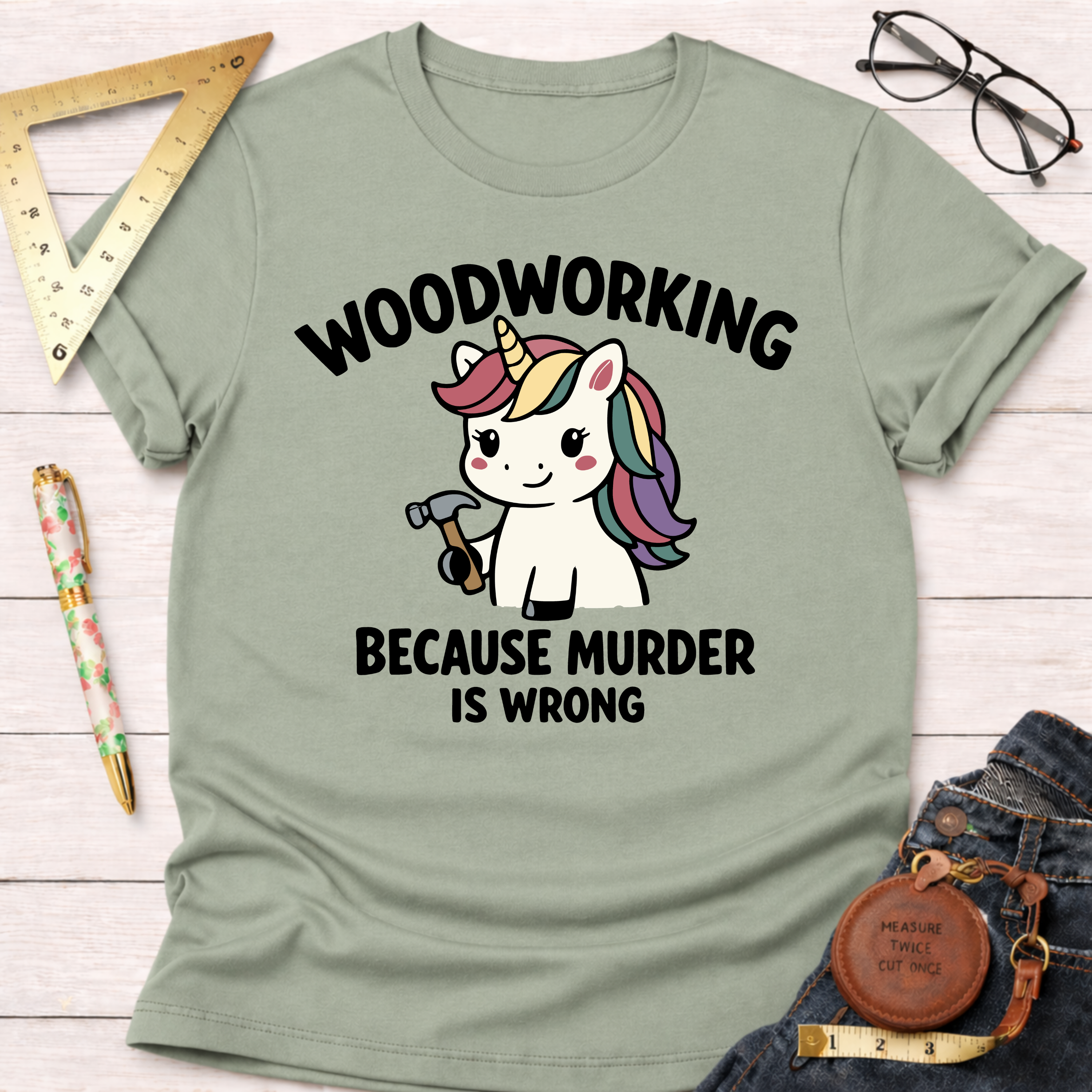 Women's funny woodworking graphic tee shirt for female woodworkers, makers, and DIY builders — Sawdust & Ponytails. Light green t-shirt with "Woodworking Because Murder Is Wrong" text and a unicorn holding a hammer.