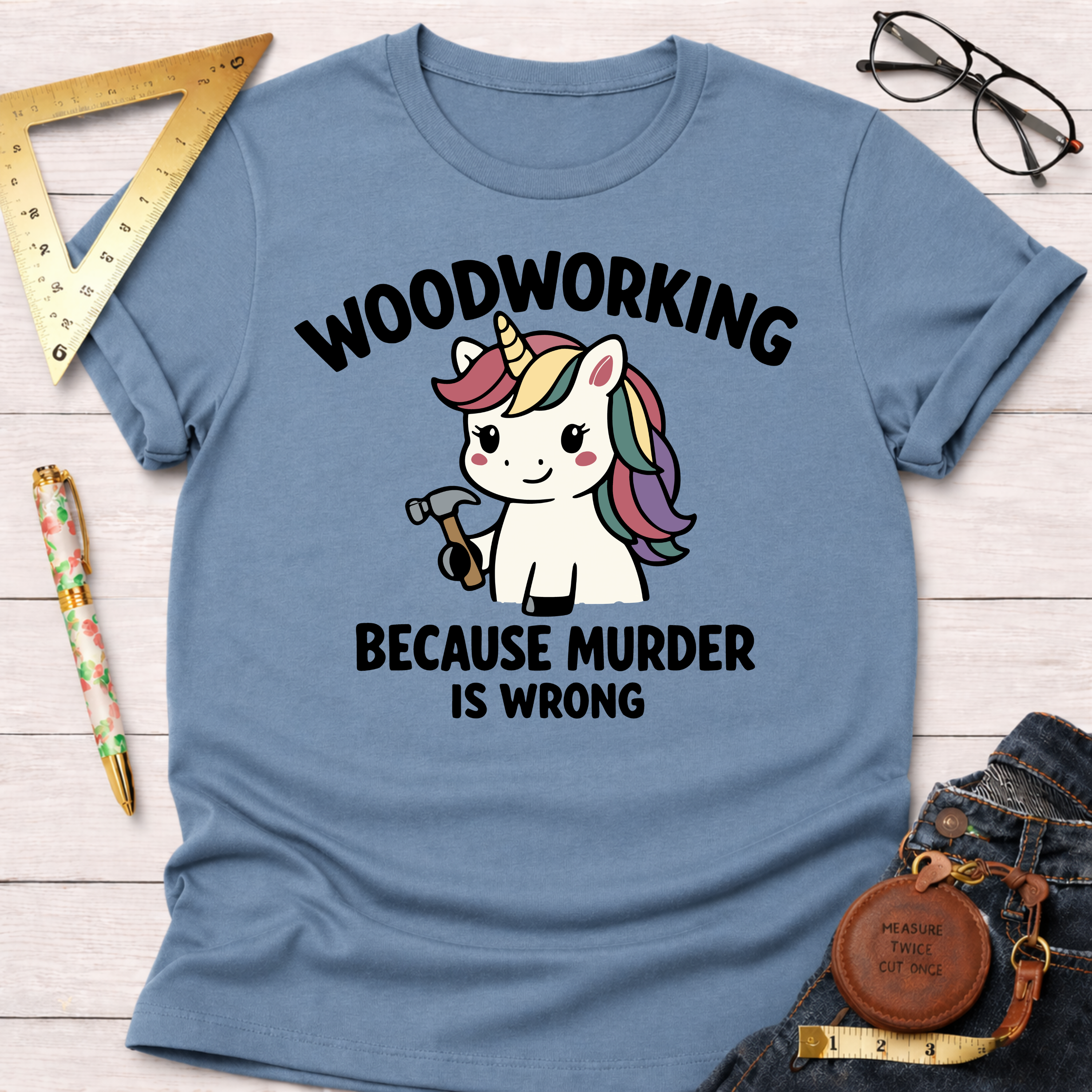 Women's funny woodworking graphic tee shirt for female woodworkers, makers, and DIY builders — Sawdust & Ponytails. Light blue cotton tee with "Woodworking Because Murder Is Wrong" and a unicorn holding a hammer.