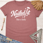 Women's funny woodworking graphic tee shirt for female woodworkers, makers, and DIY builders — Sawdust & Ponytails. Mauve t-shirt with "Nailed It like a lady" in white script.