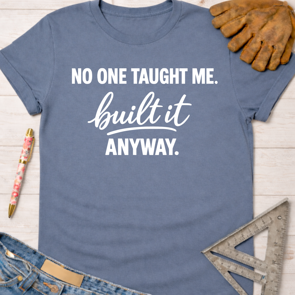 Women's funny woodworking graphic tee shirt for female woodworkers, makers, and DIY builders — Sawdust & Ponytails. Blue cotton t-shirt with "NO ONE TAUGHT ME. built it ANYWAY." in white text.