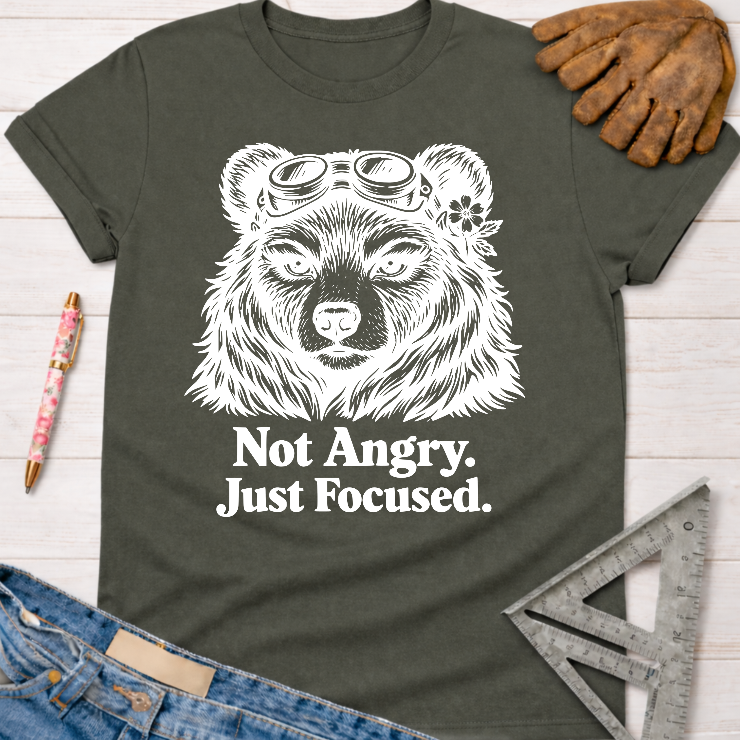 Women's funny woodworking graphic tee shirt for female woodworkers, makers, and DIY builders — Sawdust & Ponytails. Dark gray cotton tee with white "Not Angry. Just Focused." text and a bear wearing goggles and a flower.