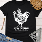 Women's funny woodworking graphic tee shirt for female woodworkers, makers, and DIY builders — Sawdust & Ponytails. Black cotton tee with white graphic of a raccoon riding a rooster, "Living The Dream One Bad Cut At A Time.