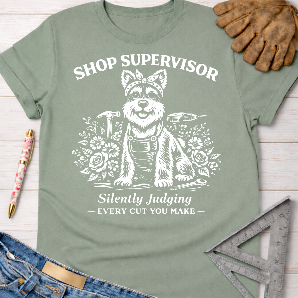 Women's funny woodworking graphic tee shirt for female woodworkers, makers, and DIY builders — Sawdust & Ponytails. Sage green cotton tee with "Shop Supervisor Silently Judging" text and a dog in overalls surrounded by tools and flowers.