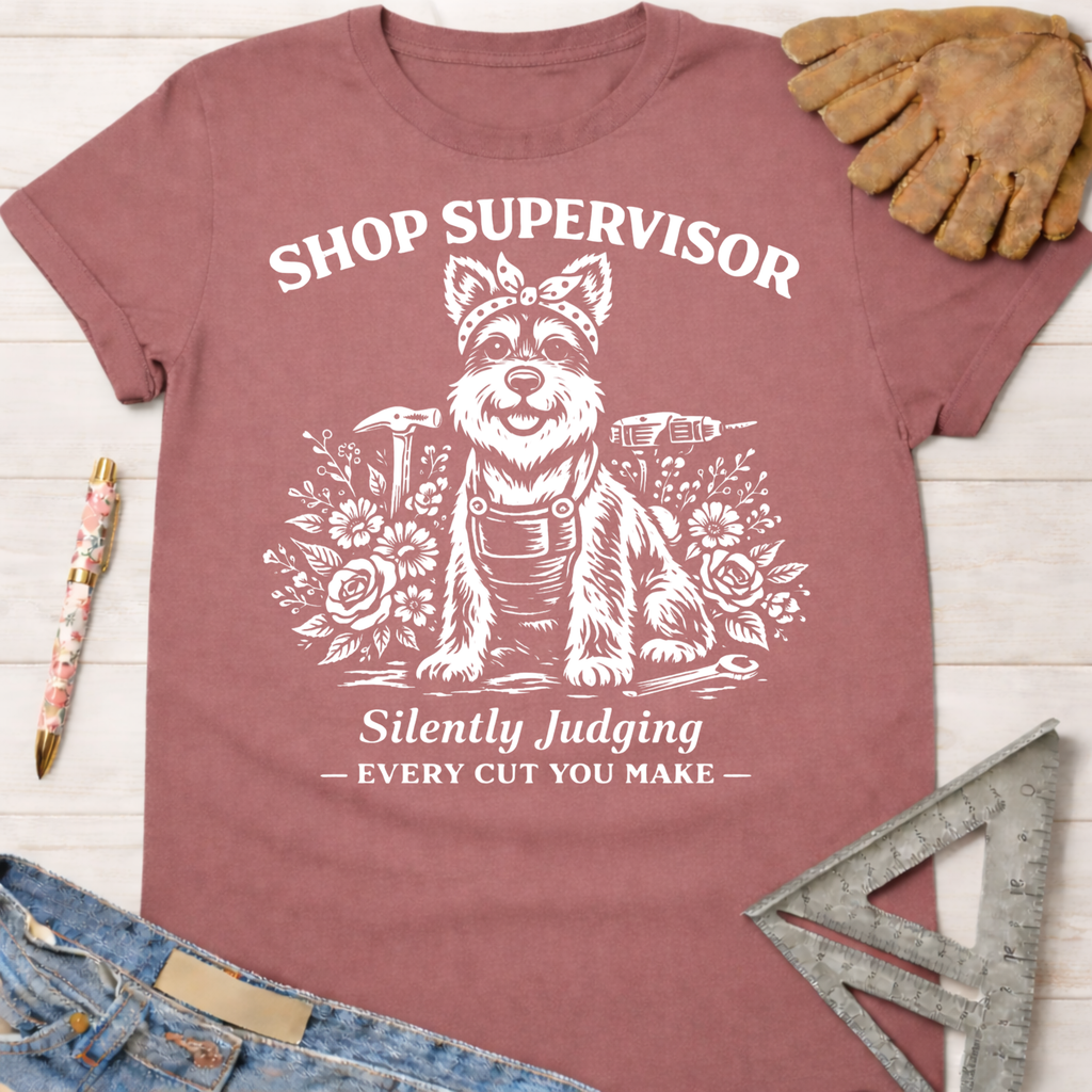 Women's funny woodworking graphic tee shirt for female woodworkers, makers, and DIY builders — Sawdust & Ponytails. Mauve cotton tee with white graphic of a dog in overalls, surrounded by tools and flowers, text "Shop Supervisor Silently Judging Every Cut You Make".