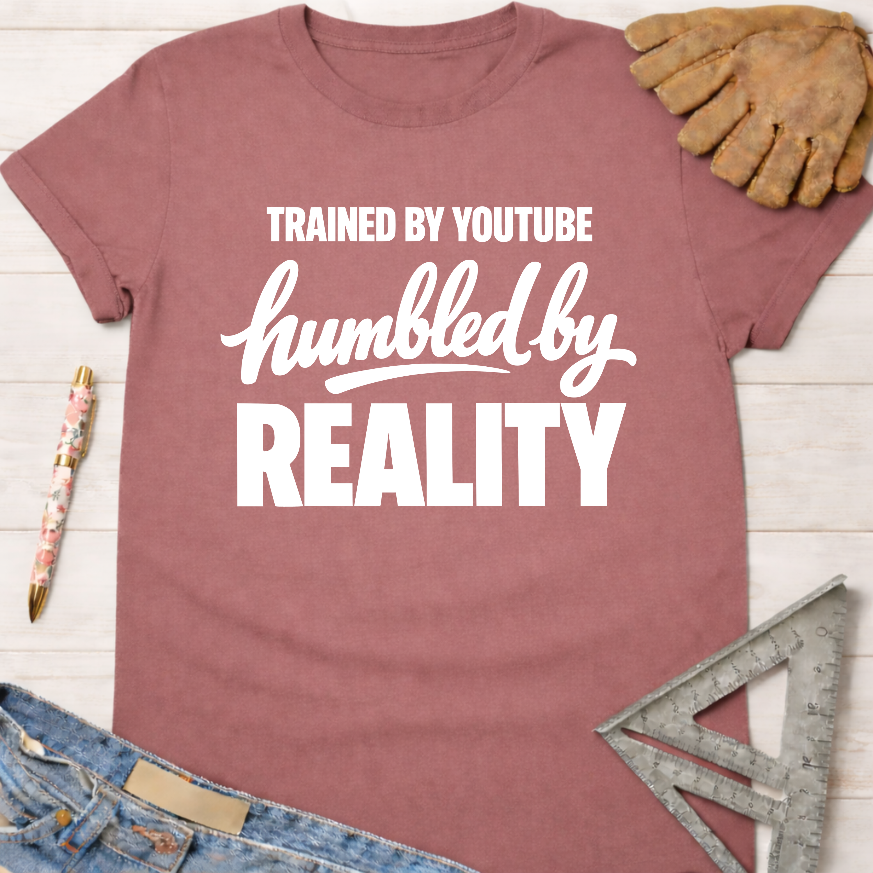Women's funny woodworking graphic tee shirt for female woodworkers, makers, and DIY builders — Sawdust & Ponytails. Mauve cotton t-shirt with "Trained By YouTube Humbled By REALITY" in white text.