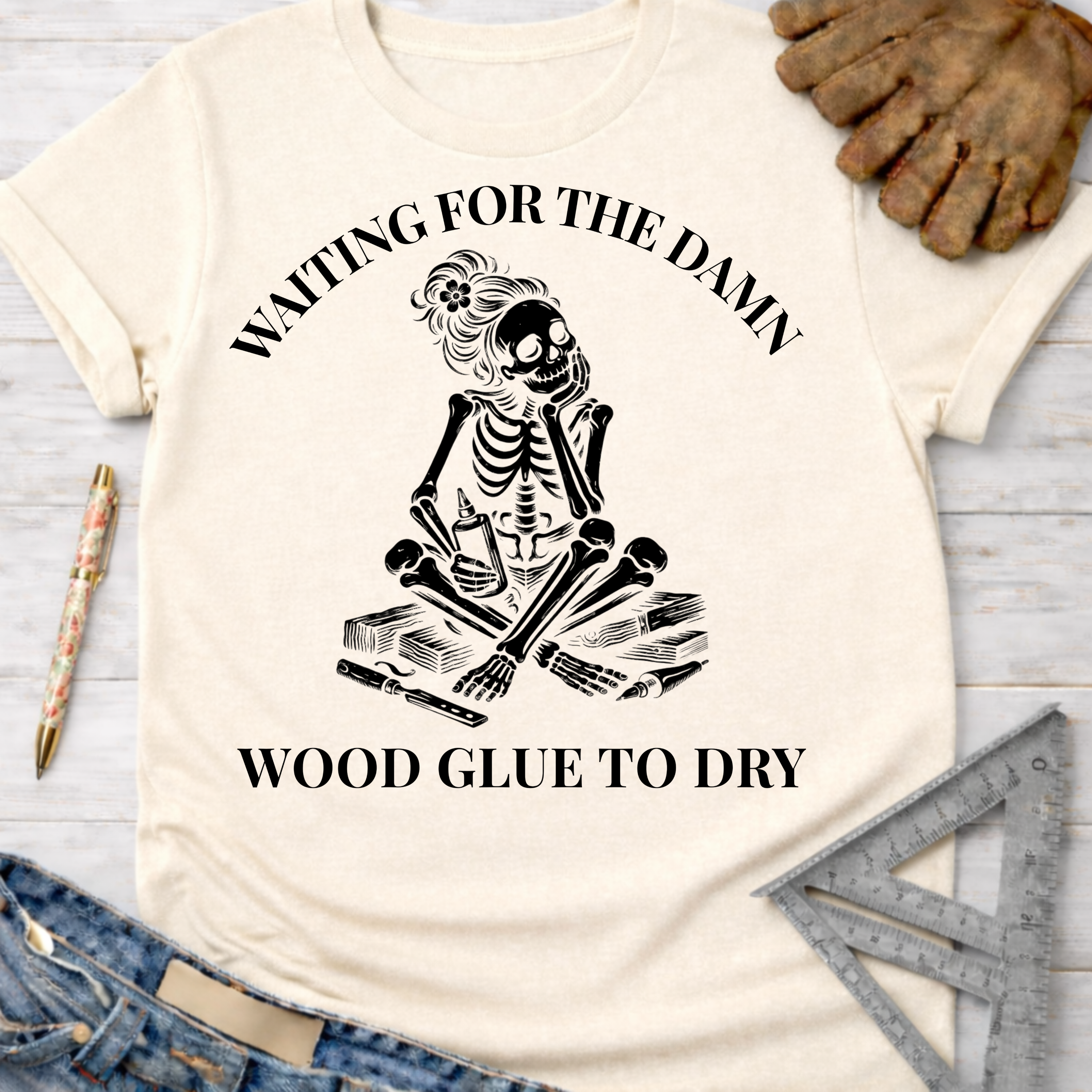 Women's funny woodworking graphic tee shirt for female woodworkers, makers, and DIY builders — Sawdust & Ponytails. Cream t-shirt with a skeleton impatiently waiting for wood glue to dry.