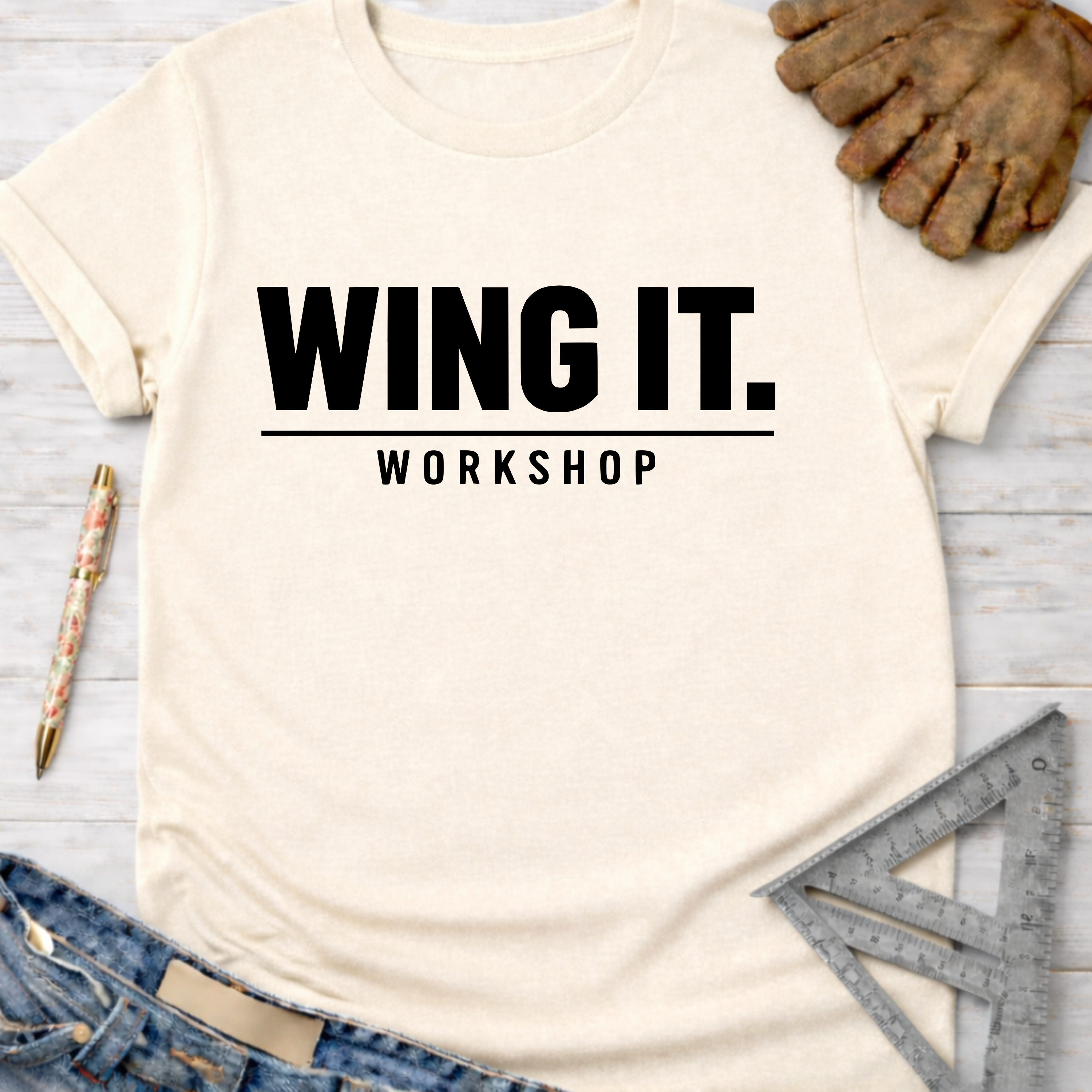 Women's funny woodworking graphic tee shirt for female woodworkers, makers, and DIY builders — Sawdust & Ponytails. Cream t-shirt with "WING IT. WORKSHOP" in black text, styled with jeans, work gloves, and tools.