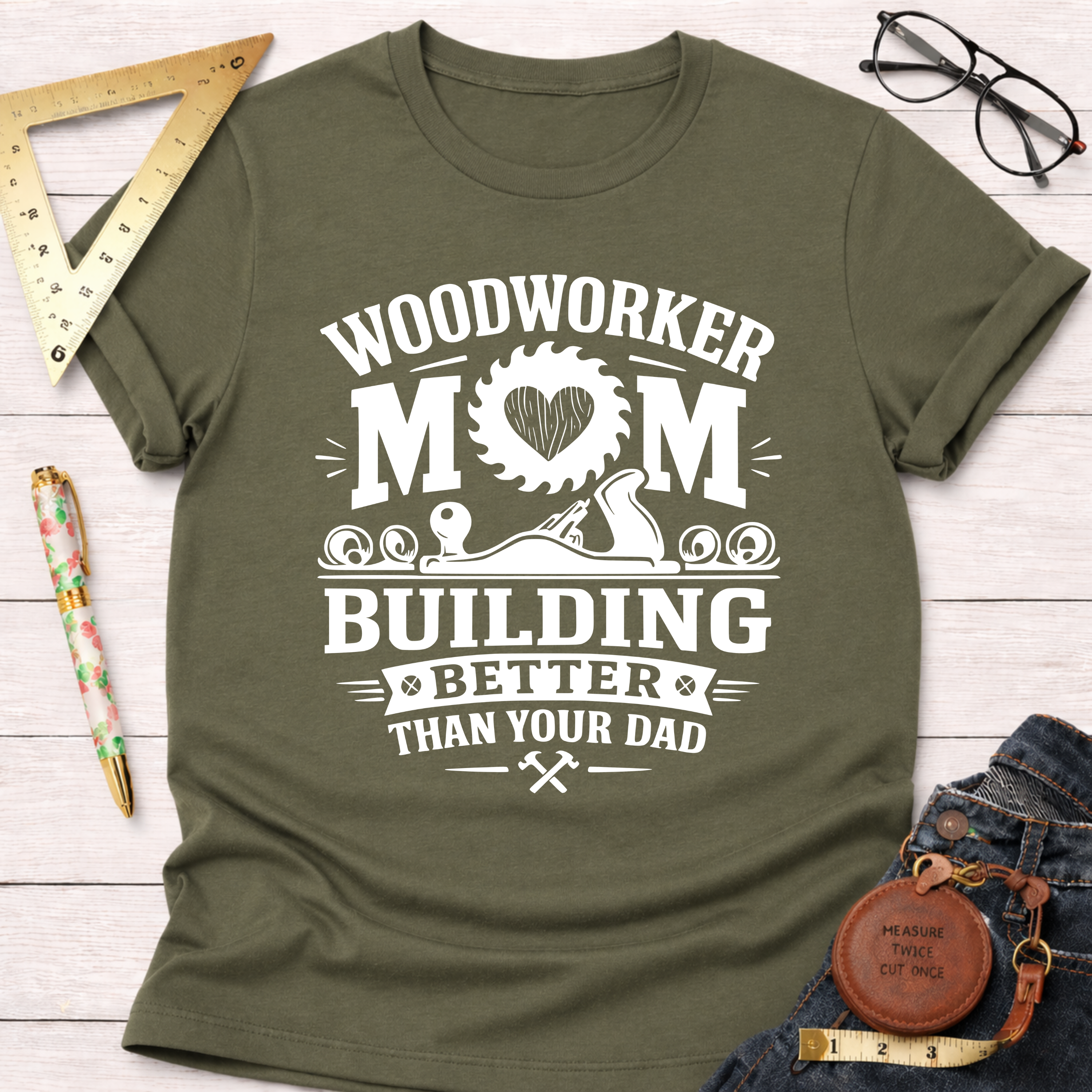 Women's funny woodworking graphic tee shirt for female woodworkers, makers, and DIY builders — Sawdust & Ponytails. Olive green cotton tee with "Woodworker Mom Building Better Than Your Dad" graphic.