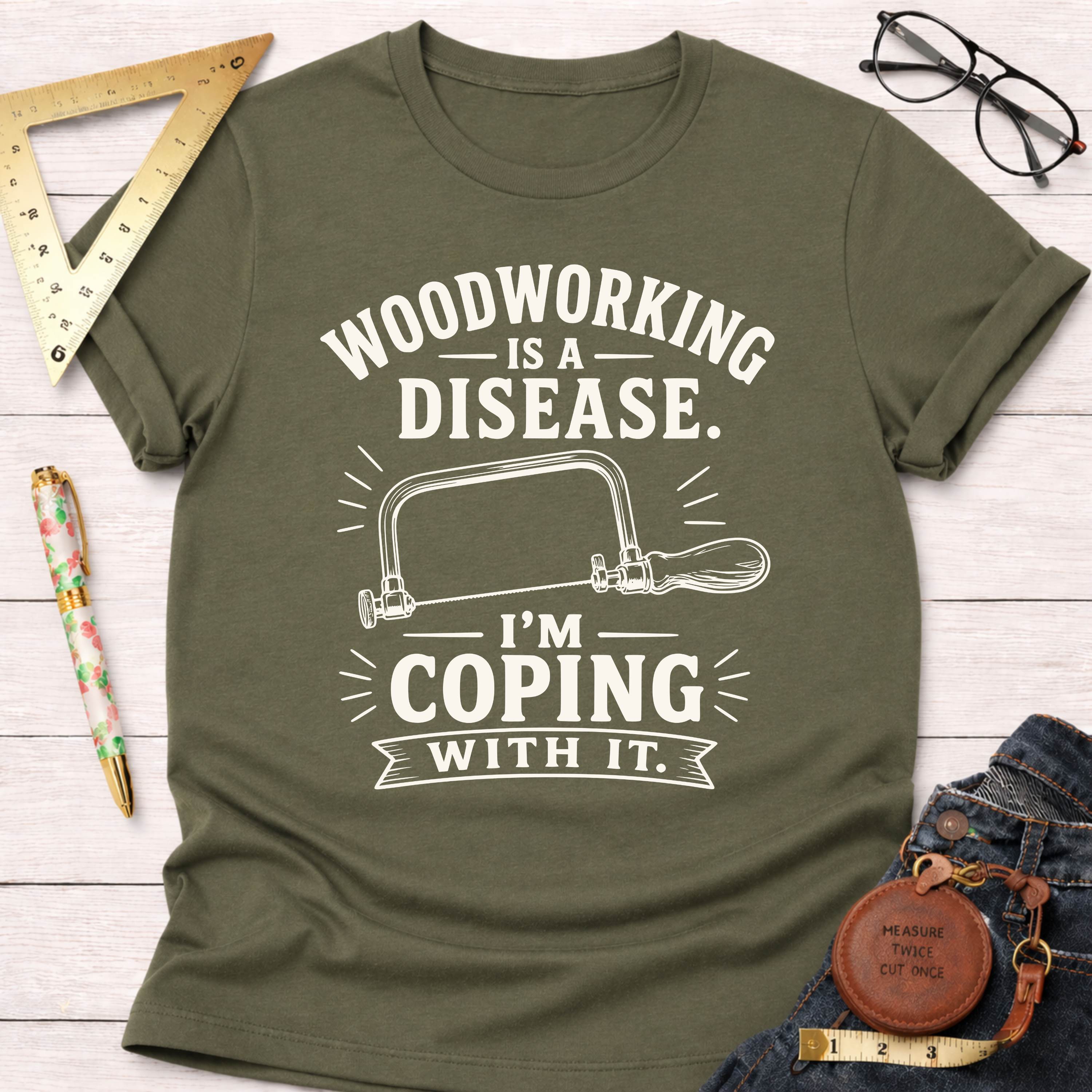 Women's funny woodworking graphic tee shirt for female woodworkers, makers, and DIY builders — Sawdust & Ponytails. Olive green cotton tee with "Woodworking Is A Disease. I'm Coping With It." text and hand saw graphic.